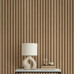 A modern interior featuring Wooden Pillar Wallpaper with vertical grooves in a warm wood tone. The wallpaper adds texture and depth to the space, complemented by a white table lamp with a sculptural base on a sleek black and white console table.
