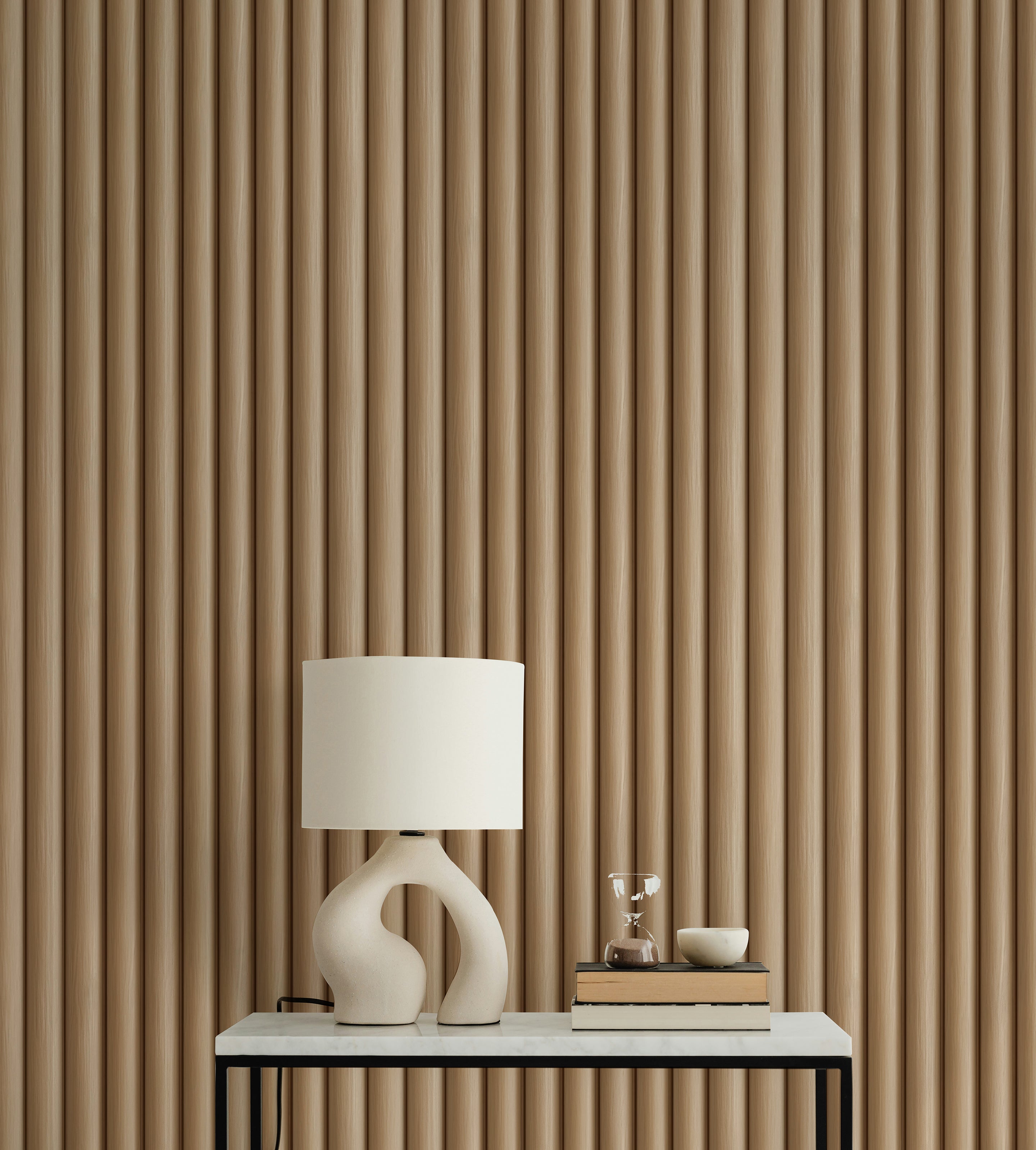 A modern interior featuring Wooden Pillar Wallpaper with vertical grooves in a warm wood tone. The wallpaper adds texture and depth to the space, complemented by a white table lamp with a sculptural base on a sleek black and white console table.