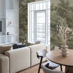 A bright and airy living room corner with a comfortable beige sofa and wooden chairs, looking out to a balcony. The wall is covered by the 'Landscape in Eext' mural, providing a stunning backdrop of vintage greenery and tranquil nature.
