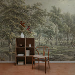A cozy reading nook with a wooden shelf and chair set against the 'Landscape in Eext' wall mural. The detailed trees and soft greenery of the mural provide a peaceful, historical ambiance to the space.