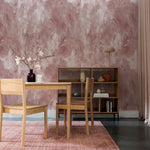 A well-appointed dining area with a modern Scandinavian aesthetic, the room features natural wood furniture and a pink textured rug, all set against the Dusty Rose Limewash Wallpaper, which adds a touch of romantic charm to the space.