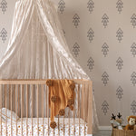 A cozy nursery room with one wall covered in Forest Animal Nursery Wallpaper. The wall features a repetitive pattern of stylized black pine trees on a soft grey backdrop, complementing the room's tranquil theme. A white crib with a sheer canopy and playful bedding enhances the nursery's soothing, woodland-inspired environment.