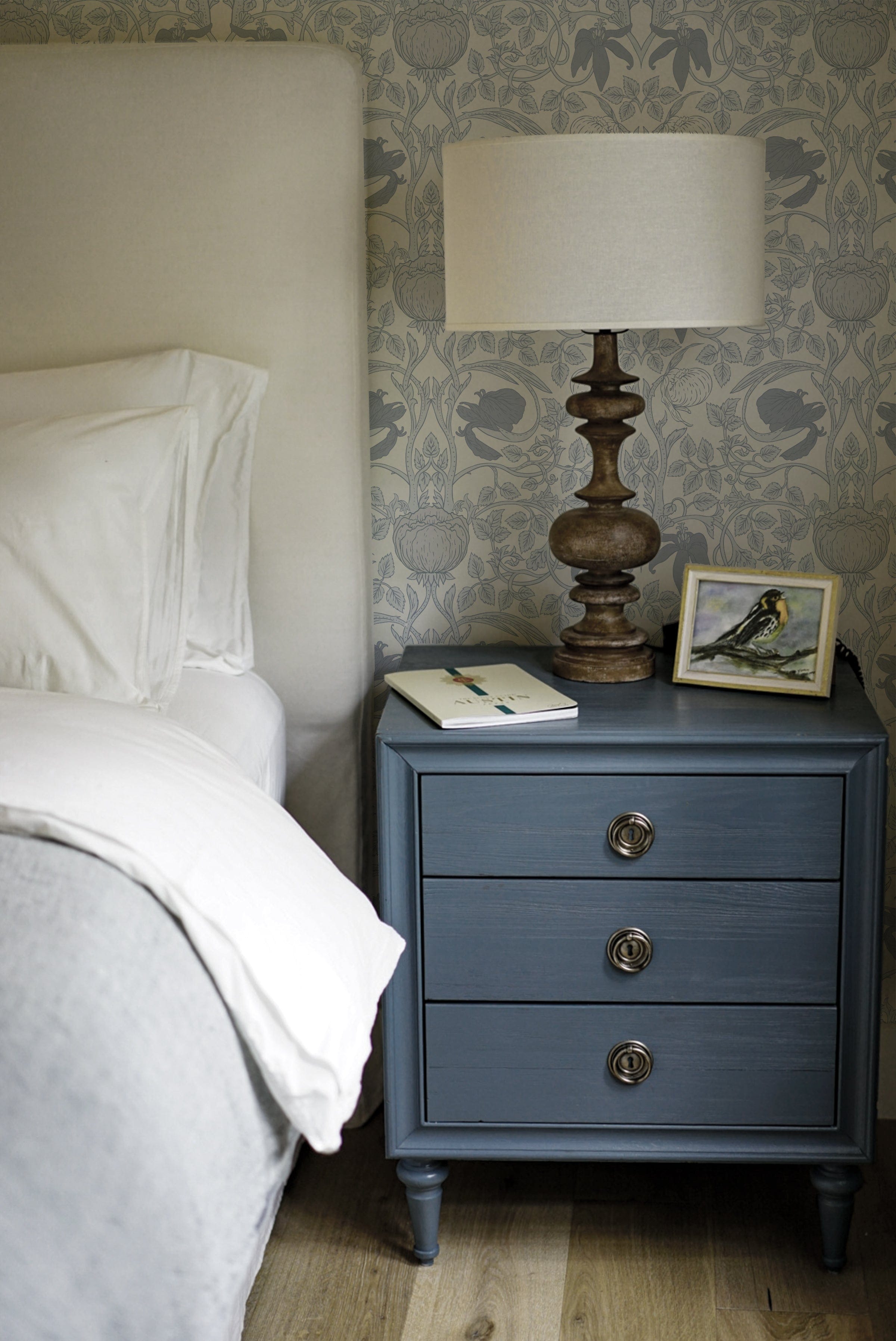 Vintage Floral Damask Wallpaper with an intricate blue floral pattern on a white background, enhancing the wall behind a blue bedside table with a lamp and a framed bird illustration in a cozy bedroom setting