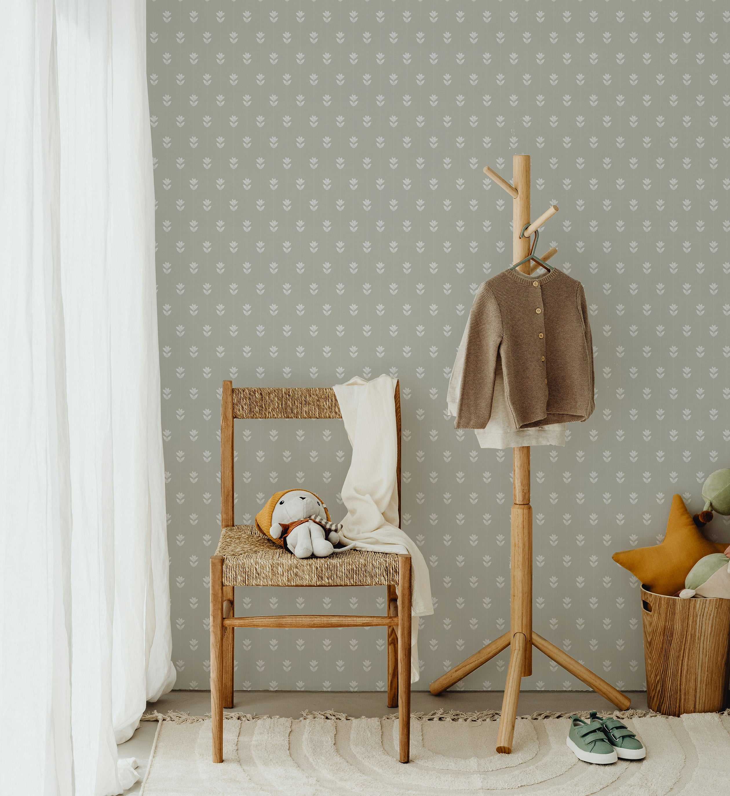 A children's corner featuring a wooden chair with a toy, a coat rack with a sweater, and a soft rug, all set against the Springtime Sprig Wallpaper. The wallpaper's gentle white sprig pattern on a green background creates a soothing and playful atmosphere.