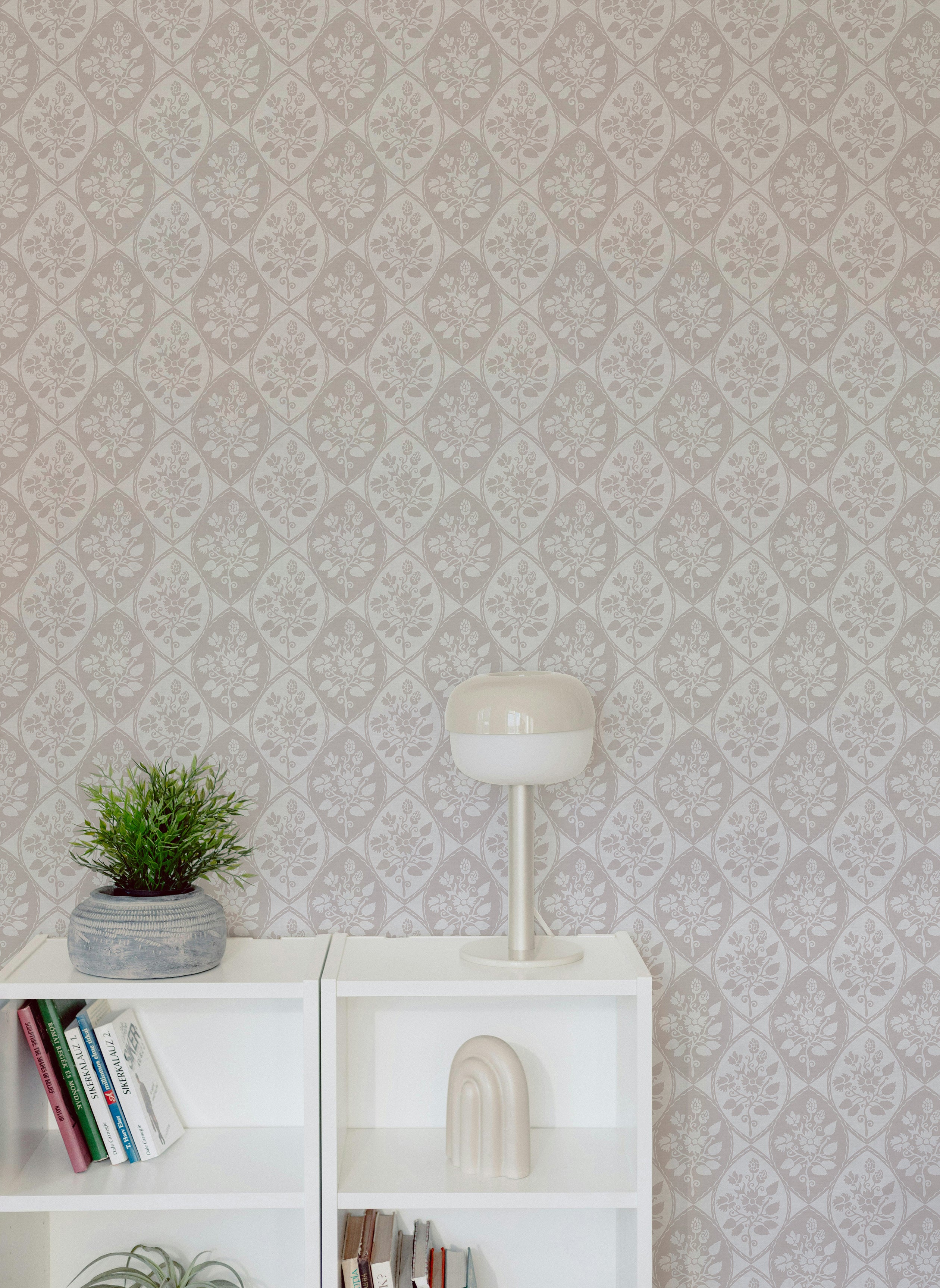 A stylish scene with white shelving, a potted plant, and a modern lamp set against the Garden Radiance Wallpaper. The wallpaper's delicate floral pattern in neutral tones enhances the contemporary yet classic aesthetic of the space.