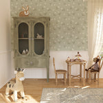 Interior view of a children's playroom with Soft Meadow Wallpaper - 25" on the feature wall. The wallpaper features a delicate pattern of small white flowers and green leaves on a soft sage background, creating a whimsical and inviting atmosphere.