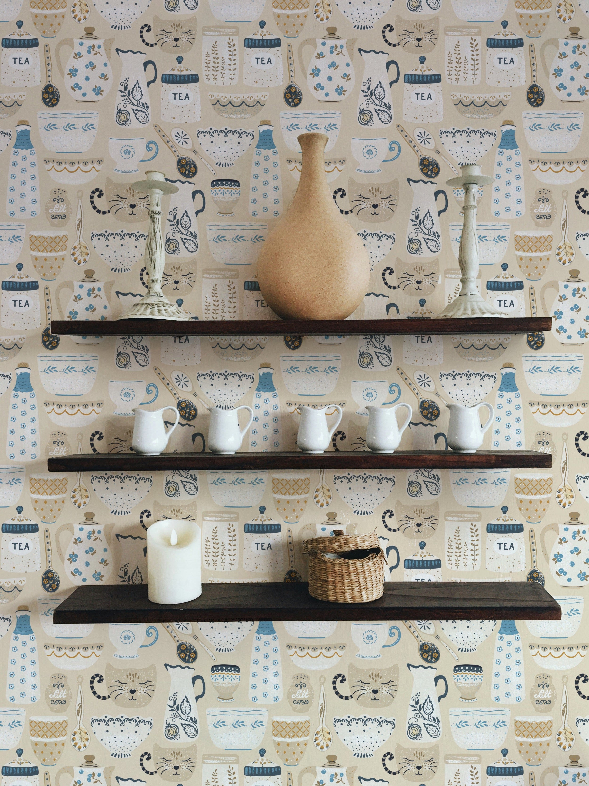 A detailed shot of a room adorned with 'Spring Ceramics Wallpaper', focusing on the wallpaper pattern featuring stylized teapots, cups, and botanical elements. The room is styled with simple, elegant decor that emphasizes the wallpaper's role as a focal point in interior design.