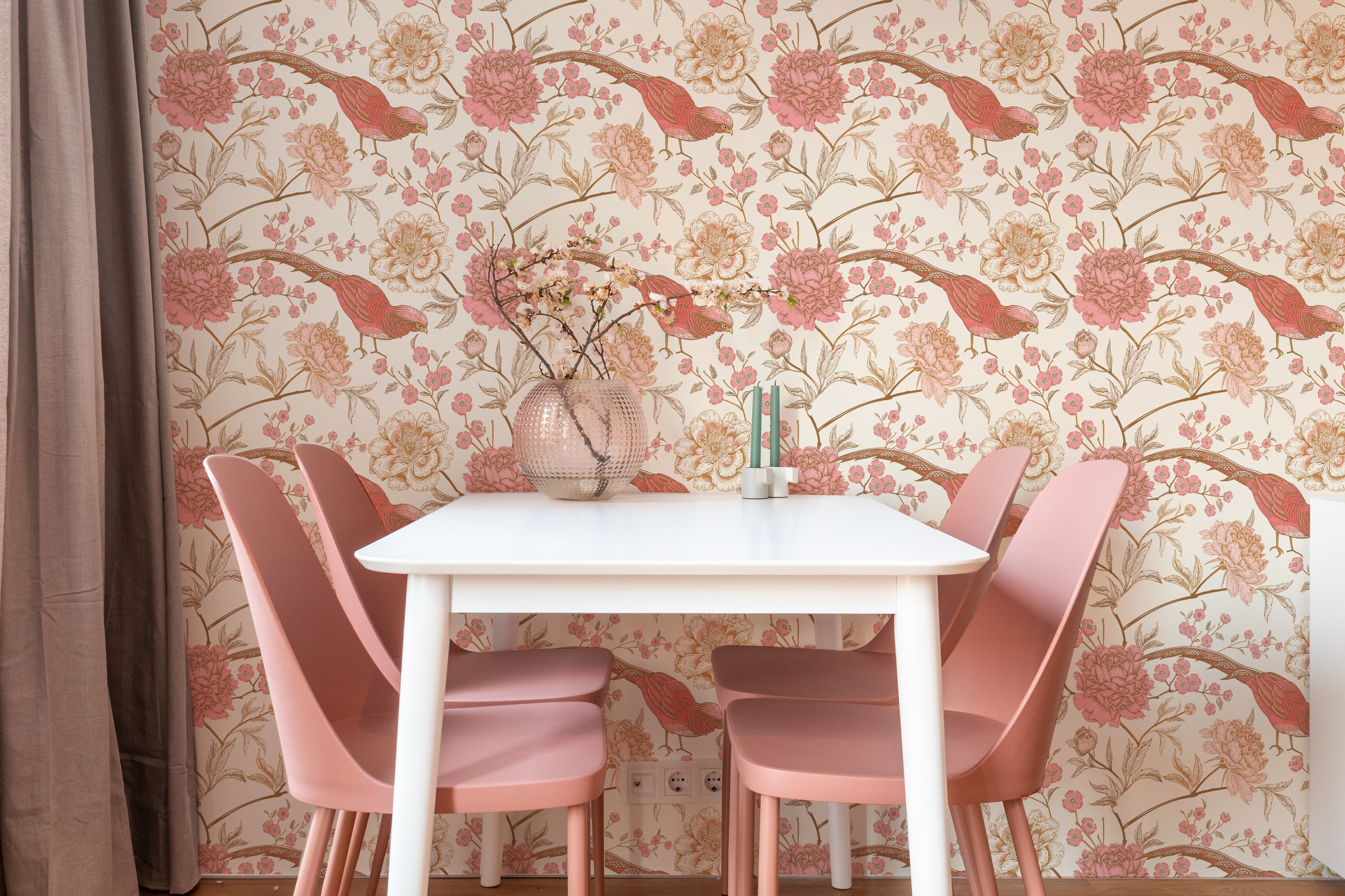 Elegant dining area featuring Peonies and Pheasants Wallpaper with a pattern of large pink peonies and red pheasants on branches, set against a cream background. The scene is complemented by a white table and pink chairs, enhancing the floral theme.
