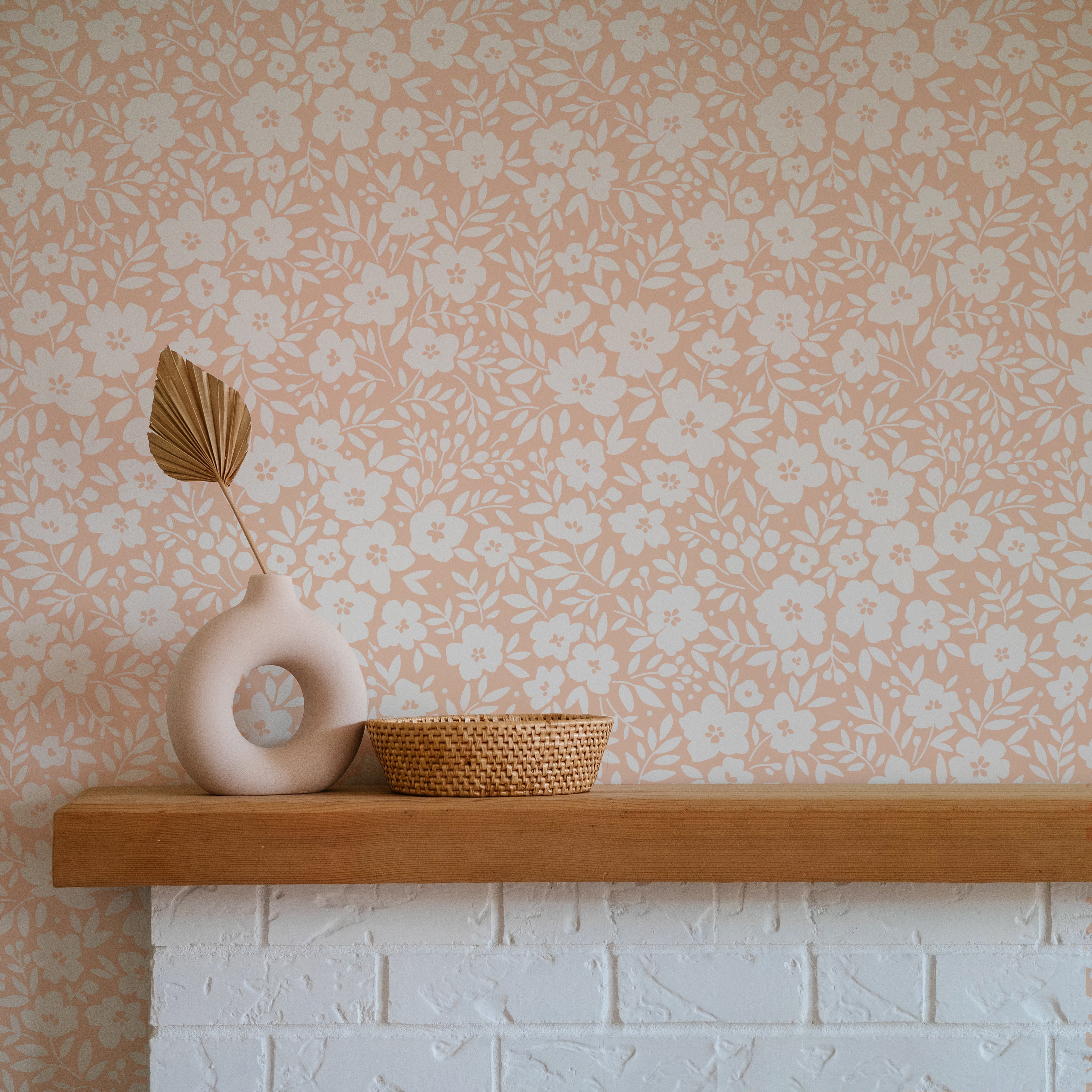 A modern and inviting space showcasing the Flower Power Wallpaper in Light Peach, featuring a dense floral pattern in light peach and white. The decor includes a contemporary vase and a woven basket on a wooden mantle, adding a rustic charm to the floral backdrop.