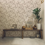 A sophisticated interior featuring Charming Floral Wallpaper in Deep Brown, showcasing an intricate pattern of small flowers and leaves. The setting includes a rustic wooden bench with decorative items, creating a warm, inviting ambiance.