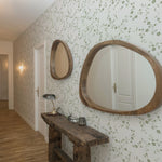 A spacious hallway is lined with the Charming Floral Wallpaper-Moss, enhancing the area with a classic, botanical charm. Two round wooden mirrors hang on the wallpapered wall above a rustic wooden bench, creating a welcoming and homey atmosphere.
