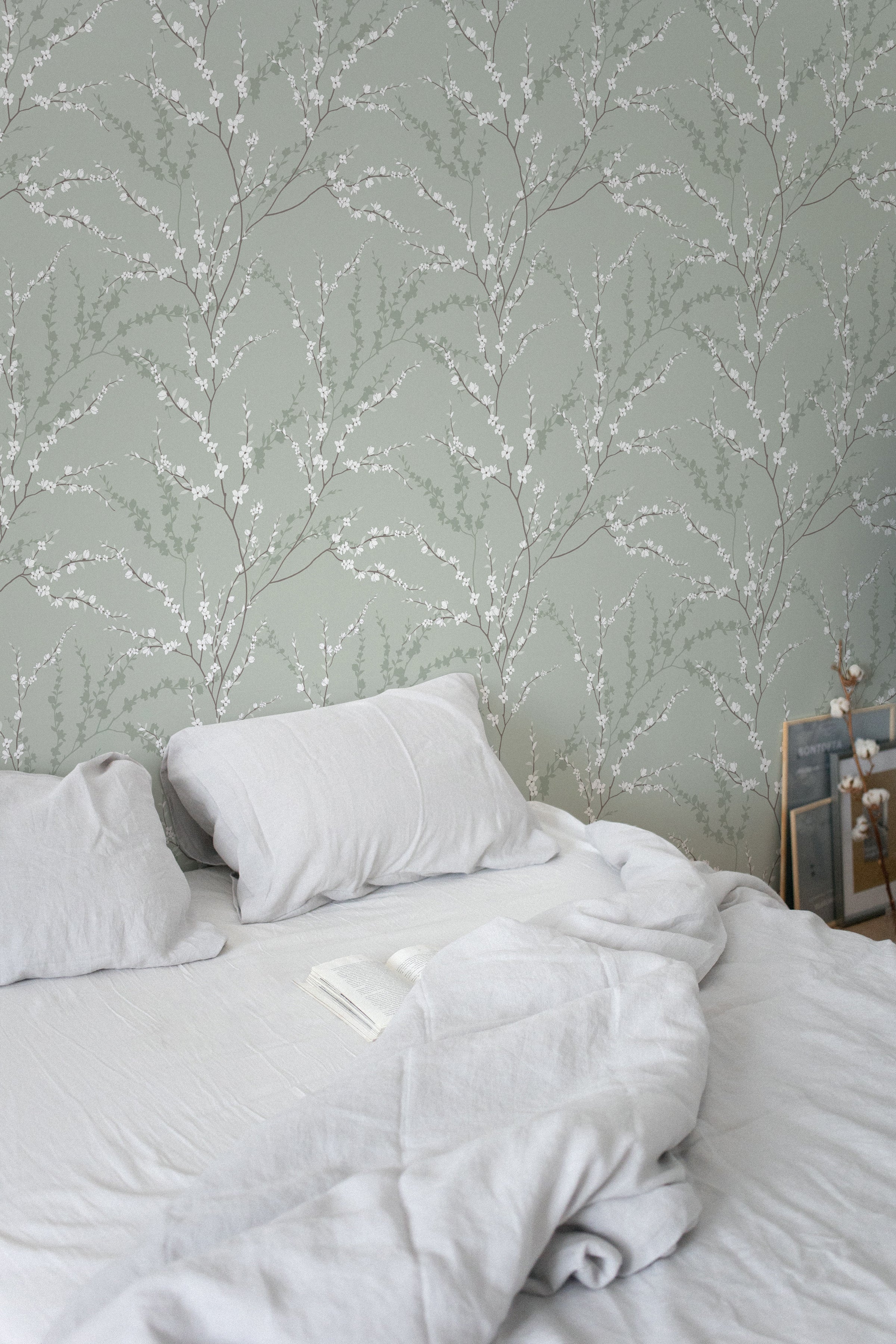 The Enchanted Blossoms Wallpaper close-up showcases the intricate detailing of white floral patterns and soft green foliage on a muted background, imparting a calming and elegant botanical aesthetic to the room.