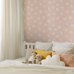  A children’s bedroom featuring the Daisy Daze Wallpaper in a soft peach tone decorated with white daisies. The room includes a bed with white bedding, several plush toys, and cushions, creating a warm and inviting atmosphere. The wallpaper adds a delightful and fresh look to the room, perfect for a child's space.