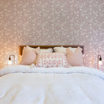 the "Whimsical Wings Wallpaper" in a warmly lit bedroom. A stylish bedside table with a minimalist lamp showcases the gentle butterfly pattern on the wallpaper, pairing beautifully with the room's neutral and pastel color scheme for a peaceful sleeping space.