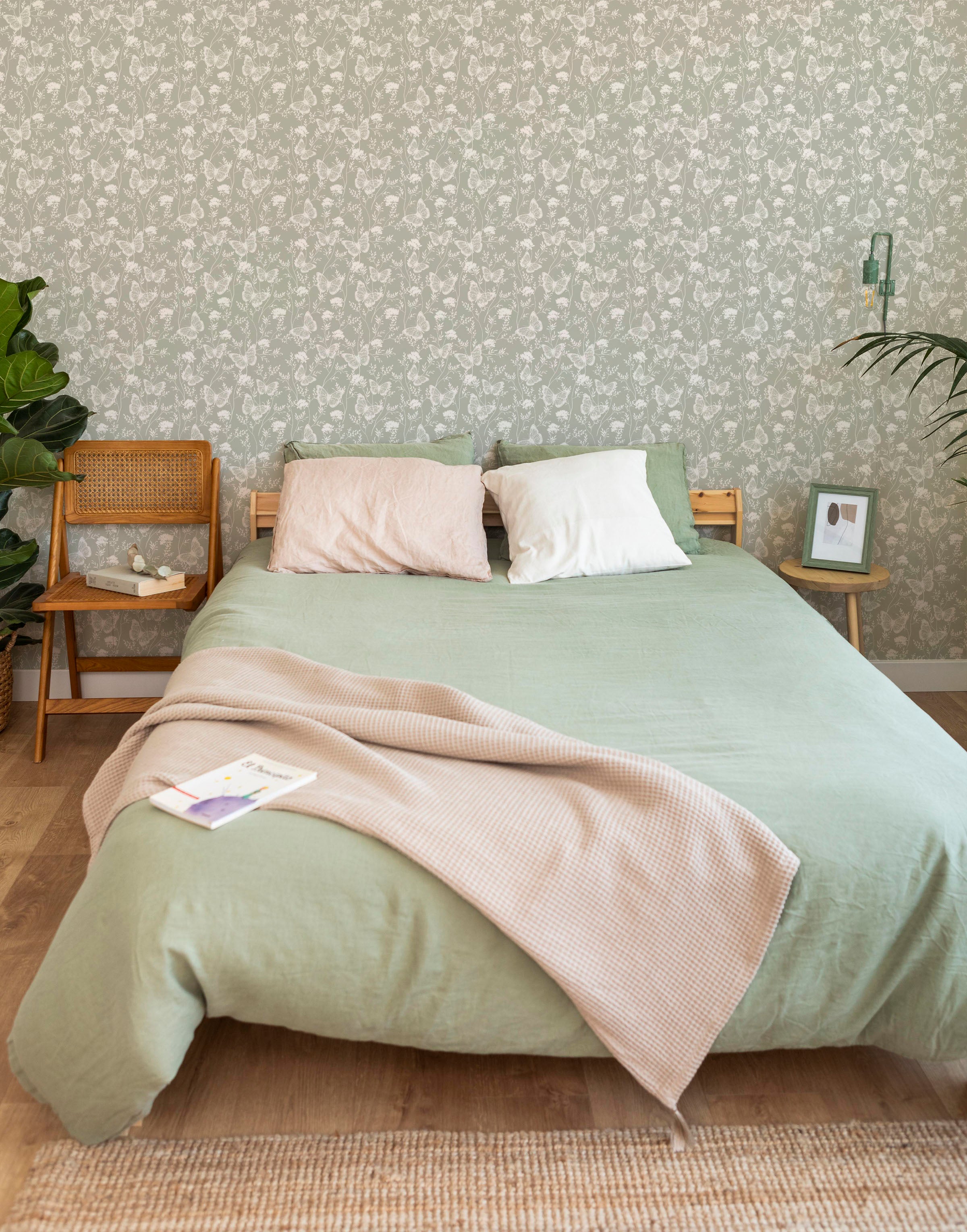 A stylish bedroom setup showing the Whimsical Wings Wallpaper-Olive as a backdrop, with light-toned bedding and a minimalistic decor that complements the intricate butterfly and floral designs on the wallpaper