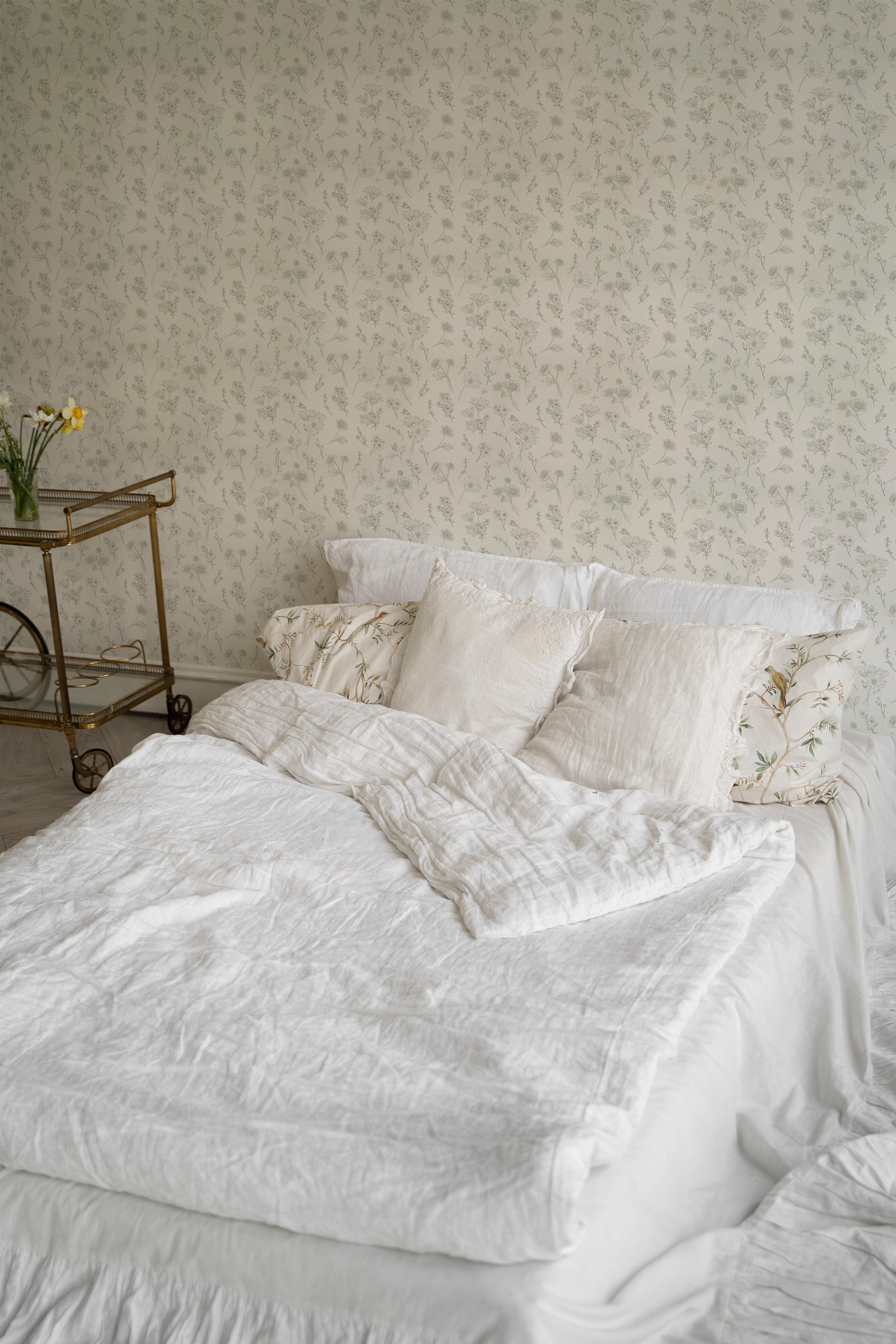 An elegant bedroom setting showcasing the Timeless Toile Wallpaper with a detailed pattern of sketched floral and botanical motifs in olive tones, adding a touch of classic sophistication to the room.