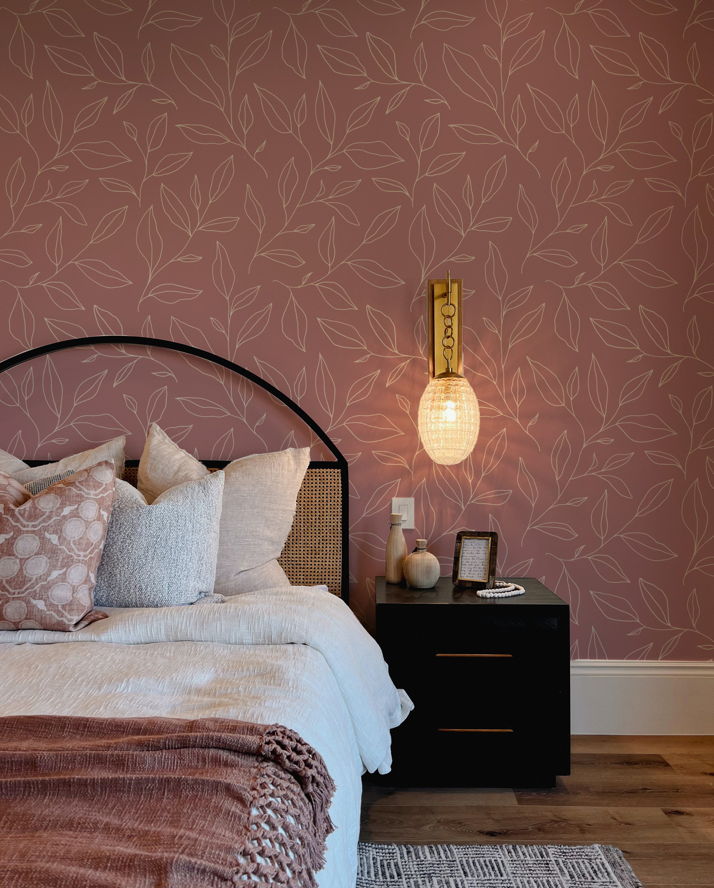 A cozy bedroom featuring the Rouge Botanicals Wallpaper with a pattern of elegant white botanical outlines on a warm rouge background, complemented by a modern black bedside table and stylish bedding.
