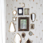 An artistic wall arrangement of variously shaped vintage mirrors reflecting different angles of the room, set against 'Muted Floral Wallpaper' with subtle floral designs that evoke a sense of calm elegance.
