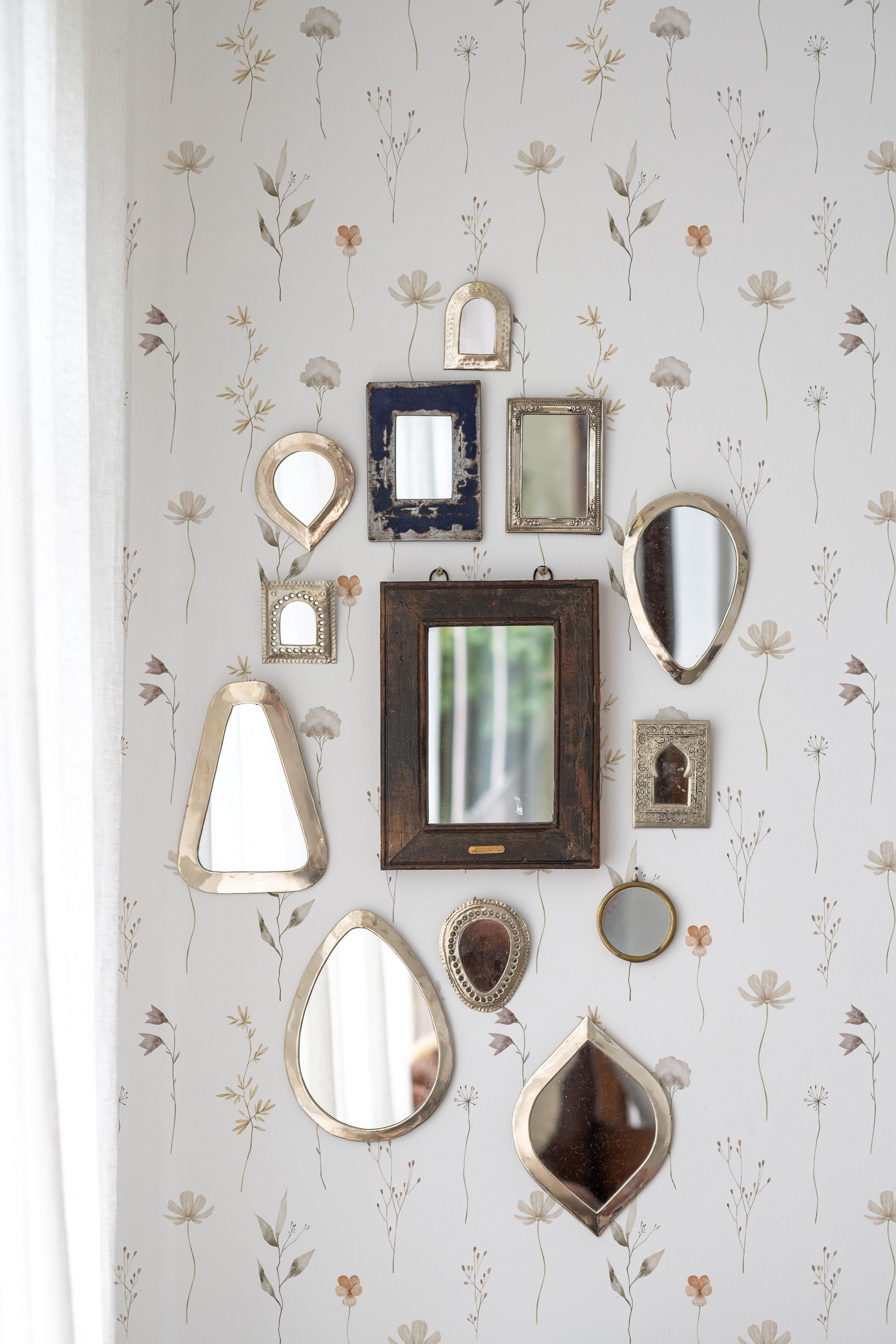 An artistic wall arrangement of variously shaped vintage mirrors reflecting different angles of the room, set against 'Muted Floral Wallpaper' with subtle floral designs that evoke a sense of calm elegance.