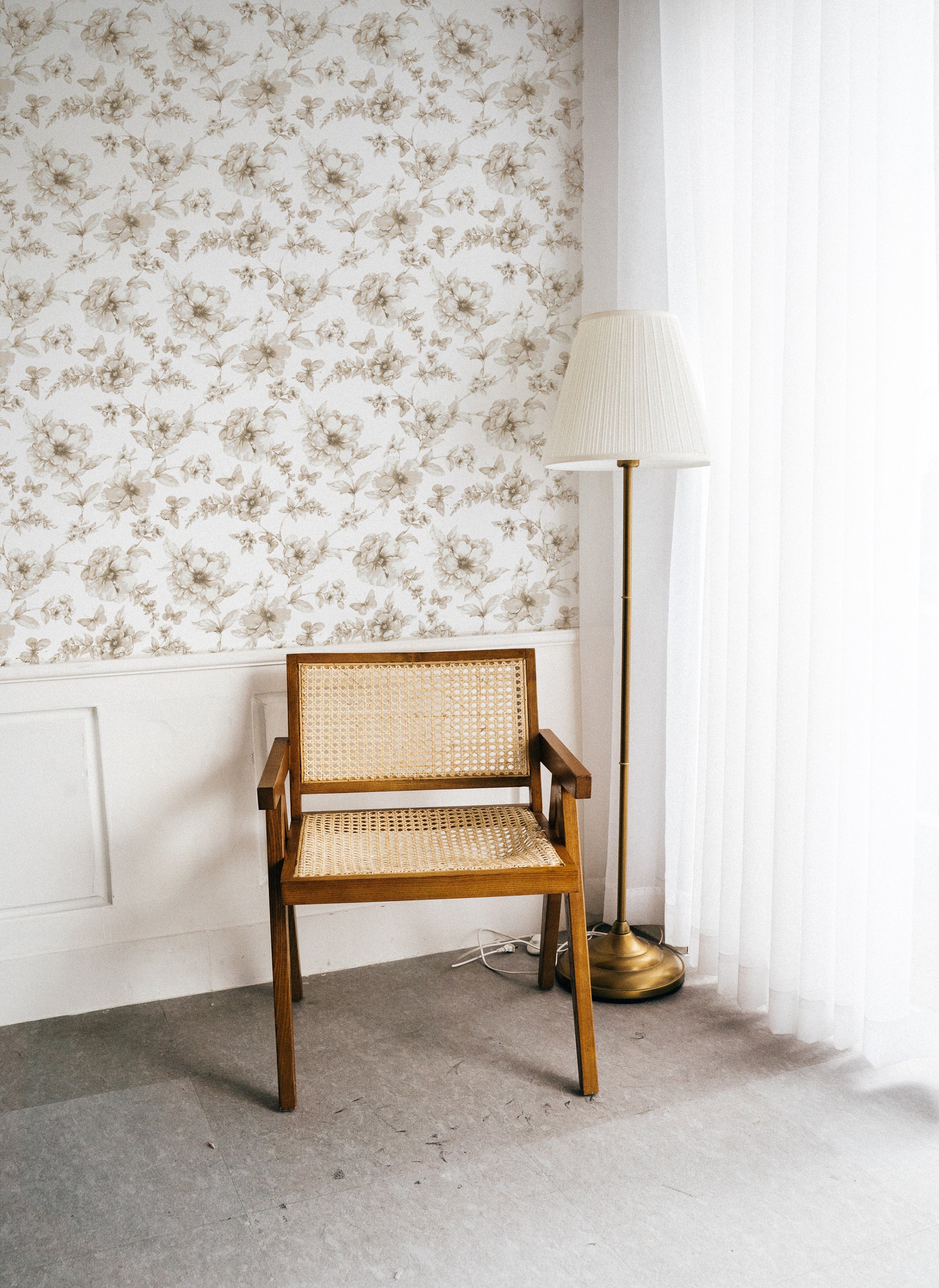 A minimalist setup featuring the Sepia Trellis Wallpaper in a bright room with natural light. The wallpaper provides a delicate backdrop to a vintage wooden chair and a tall floor lamp, enhancing the serene and elegant atmosphere.