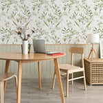 An elegant work area with the 'Botanical Bliss Wallpaper' gracing the wall, featuring a sophisticated pattern of soft green botanicals and white blooms. The natural theme is complemented by a wooden table, chairs, decorative vases with dried plants, and a laptop, creating a harmonious and productive environment