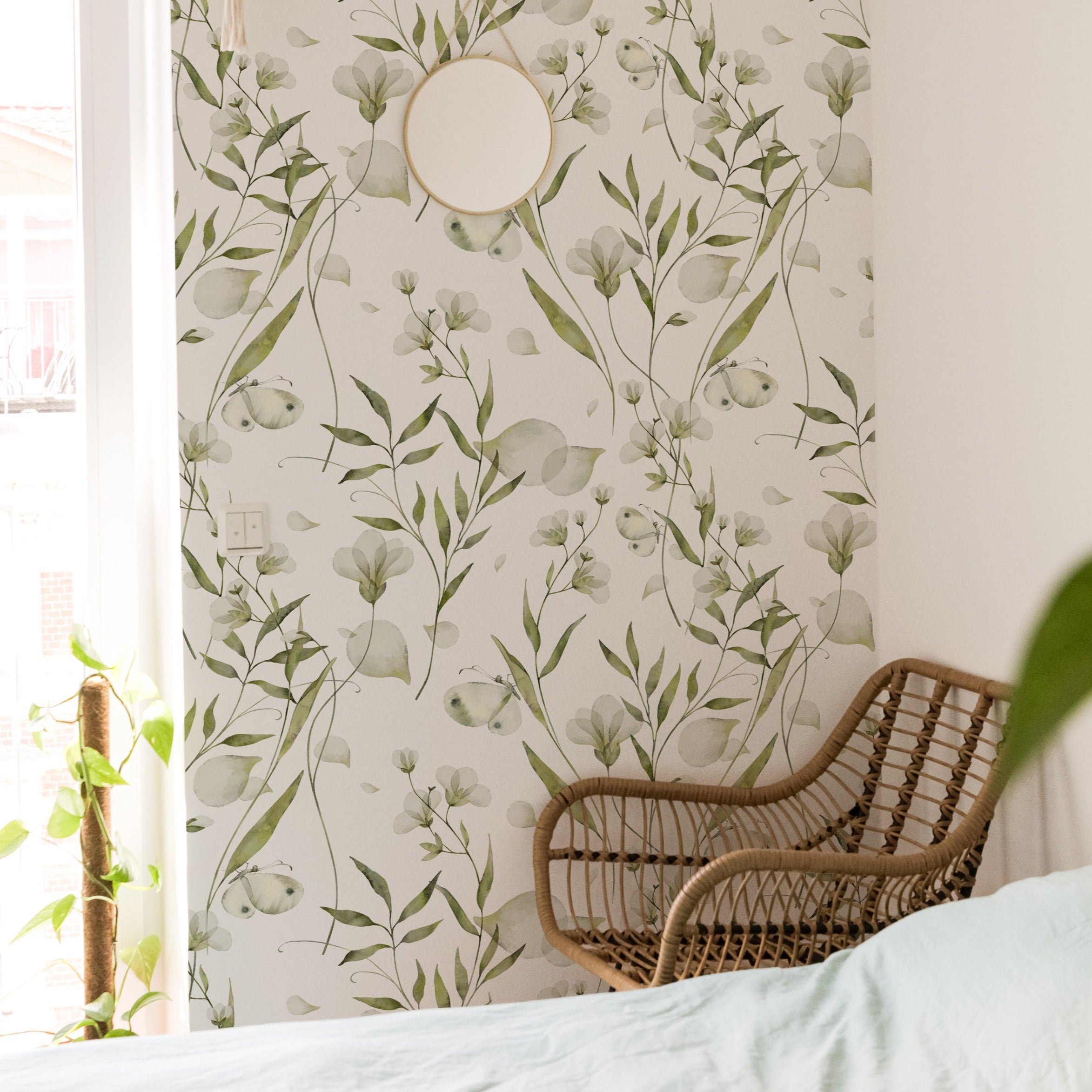 A cozy corner decorated with the 'Botanical Bliss Wallpaper,' illustrating the wallpaper's ability to create a soothing backdrop. A rattan armchair beside a bright window offers a relaxing spot, enhanced by the serene botanical pattern and the soft natural light