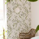 A cozy corner decorated with the 'Botanical Bliss Wallpaper,' illustrating the wallpaper's ability to create a soothing backdrop. A rattan armchair beside a bright window offers a relaxing spot, enhanced by the serene botanical pattern and the soft natural light
