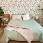 A cozy bedroom featuring the Springtime Sonata Wallpaper, adorned with a delicate pattern of pale pink tulips and lush green leaves against a white background. The elegant floral design complements the earthy tones of the green bedspread and natural wood furniture, creating a tranquil and inviting space.