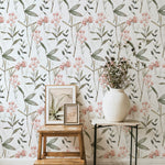 A stylishly decorated room corner with the Springtime Sonata Wallpaper. This wallpaper features a charming pattern of pink tulips and greenery, enhancing the natural aesthetic of the space, complete with a rustic wooden stool, a modern table, and a vase filled with wildflowers.