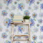 Cozy reading nook decorated with Watercolour Bliss Wallpaper, featuring large watercolor flowers. The setting includes an old white wooden ladder used as a shelf holding books and a small potted plant, adding a rustic charm to the floral decor