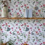Charming display on a wooden shelf against Graceful Garden Wallpaper, which is adorned with pink flowers, green leaves, and butterflies. Decor includes a rustic vase with dried cotton stems and small books.