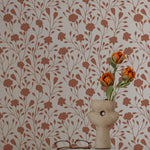 A design setting that features the Garden Gaze Wallpaper on a wall, paired with a simple home decor setup. The terracotta floral pattern against the ecru background enhances the overall aesthetic, offering a tranquil and beautiful backdrop.
