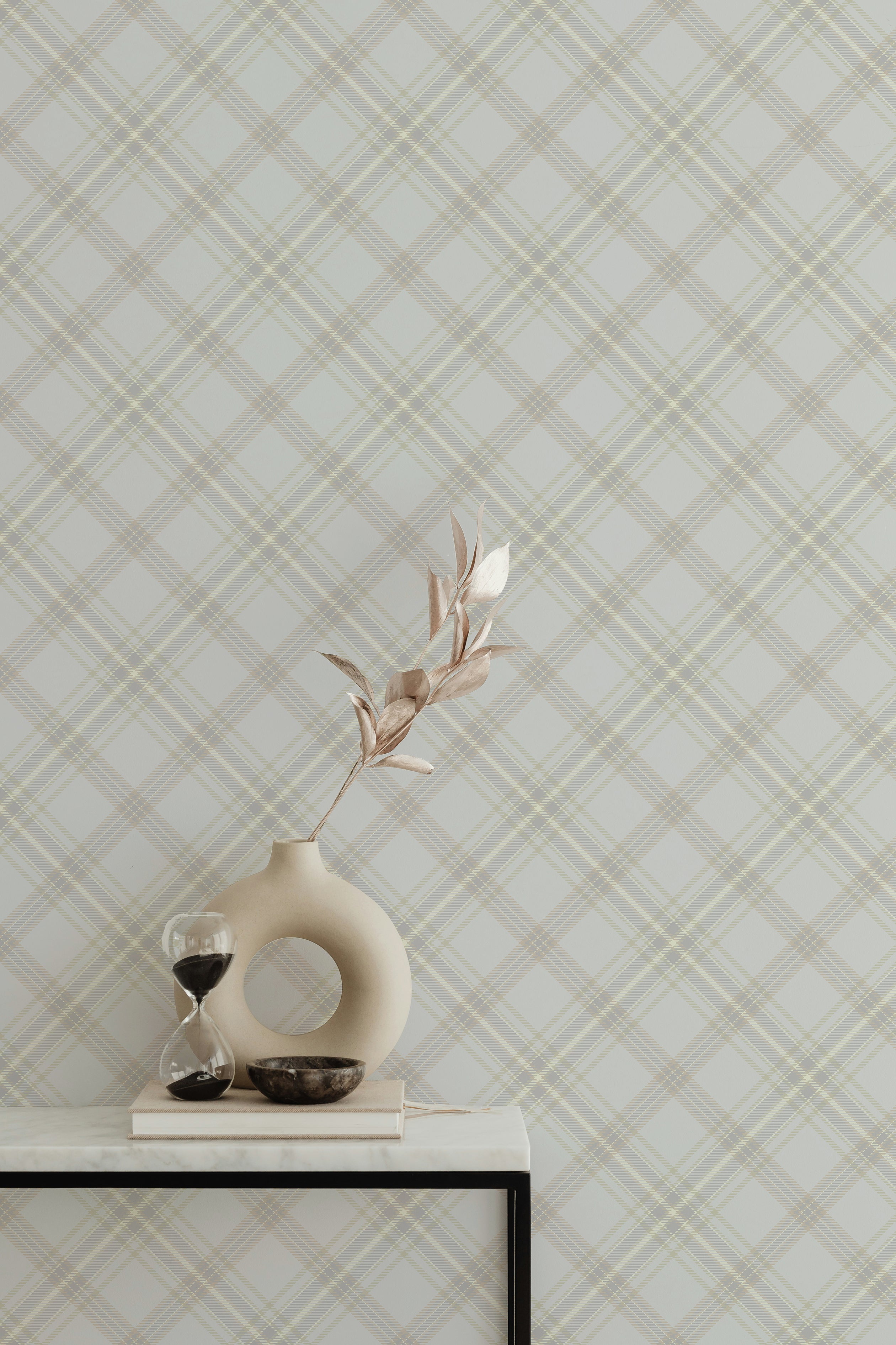 Royal Tartan Plaid Wallpaper with a classic tartan design in neutral beige and cream shades. The wallpaper adds a touch of traditional charm to the space, paired with a contemporary round vase and an hourglass timer on a sleek white table.