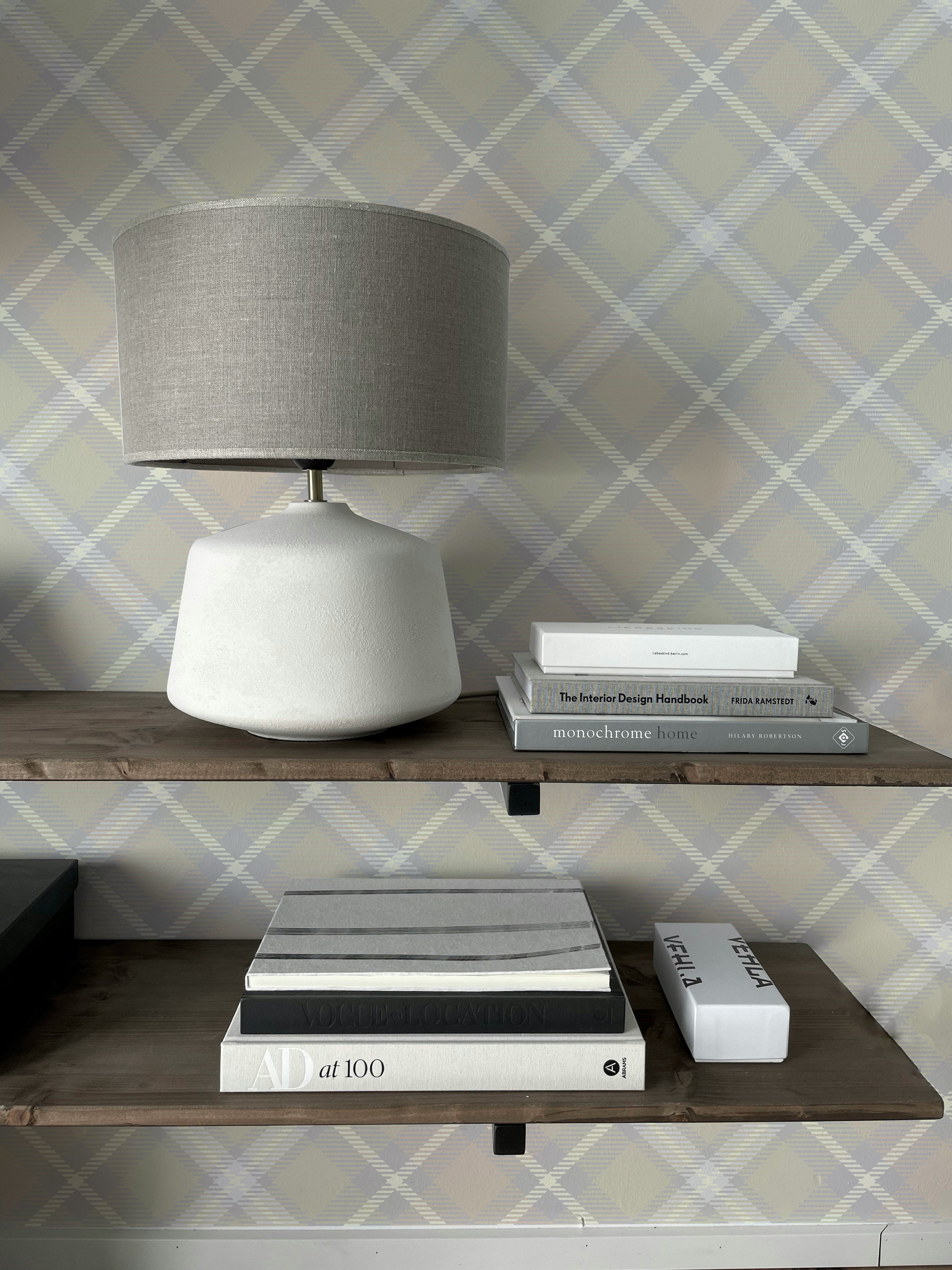 Tartan Plaid Wallpaper with a soft beige and gray crisscross pattern, providing a classic yet modern touch to the space. A minimalist lamp sits on a wooden shelf alongside neatly stacked books, enhancing the cozy and stylish ambiance of the room.