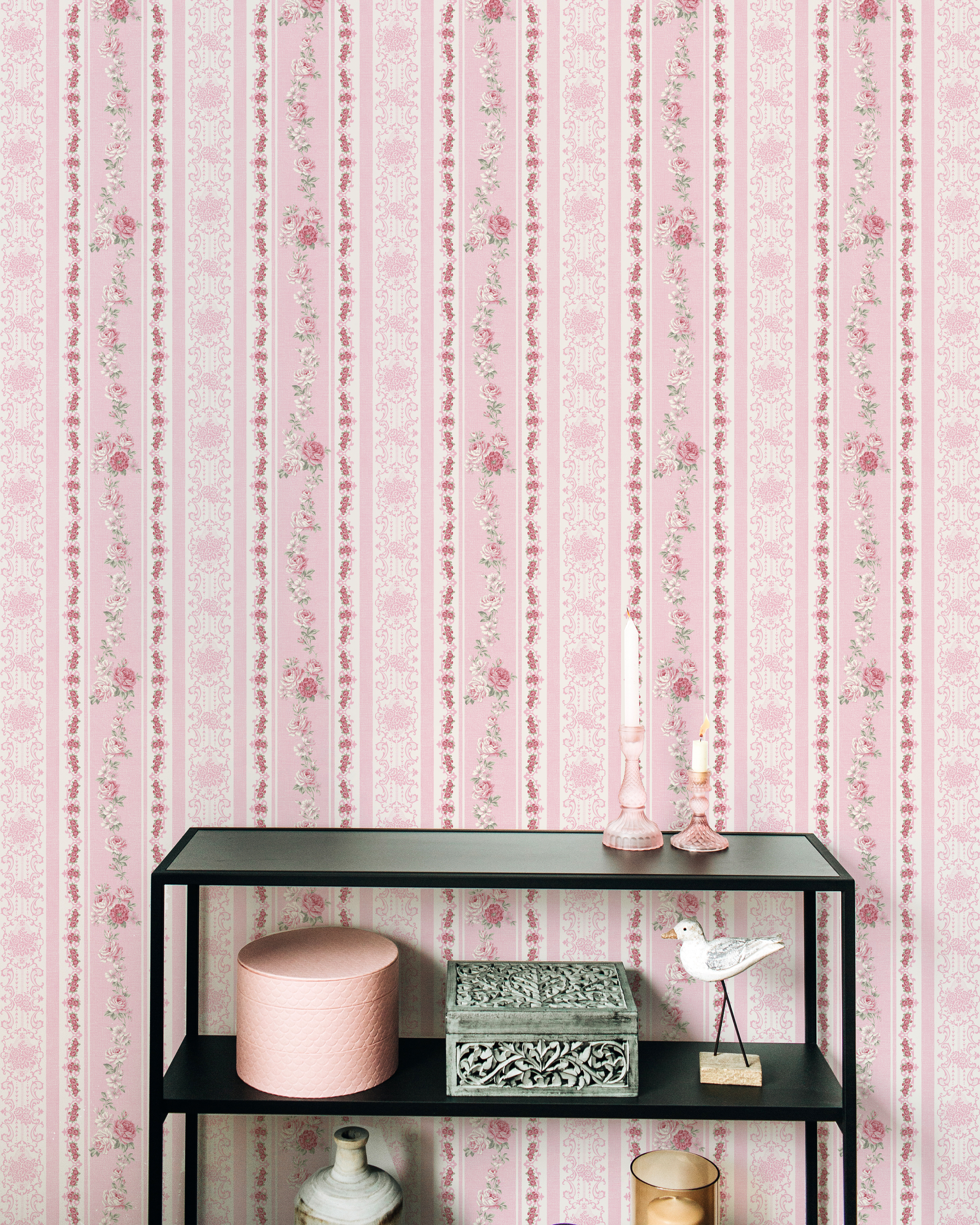 Interior scene decorated with Vintage Rose Wallpaper, featuring a modern black shelving unit against the floral and striped pink wallpaper. The shelf is styled with various decorative items including a pink box, a vintage bird figure, and pastel-colored vases.