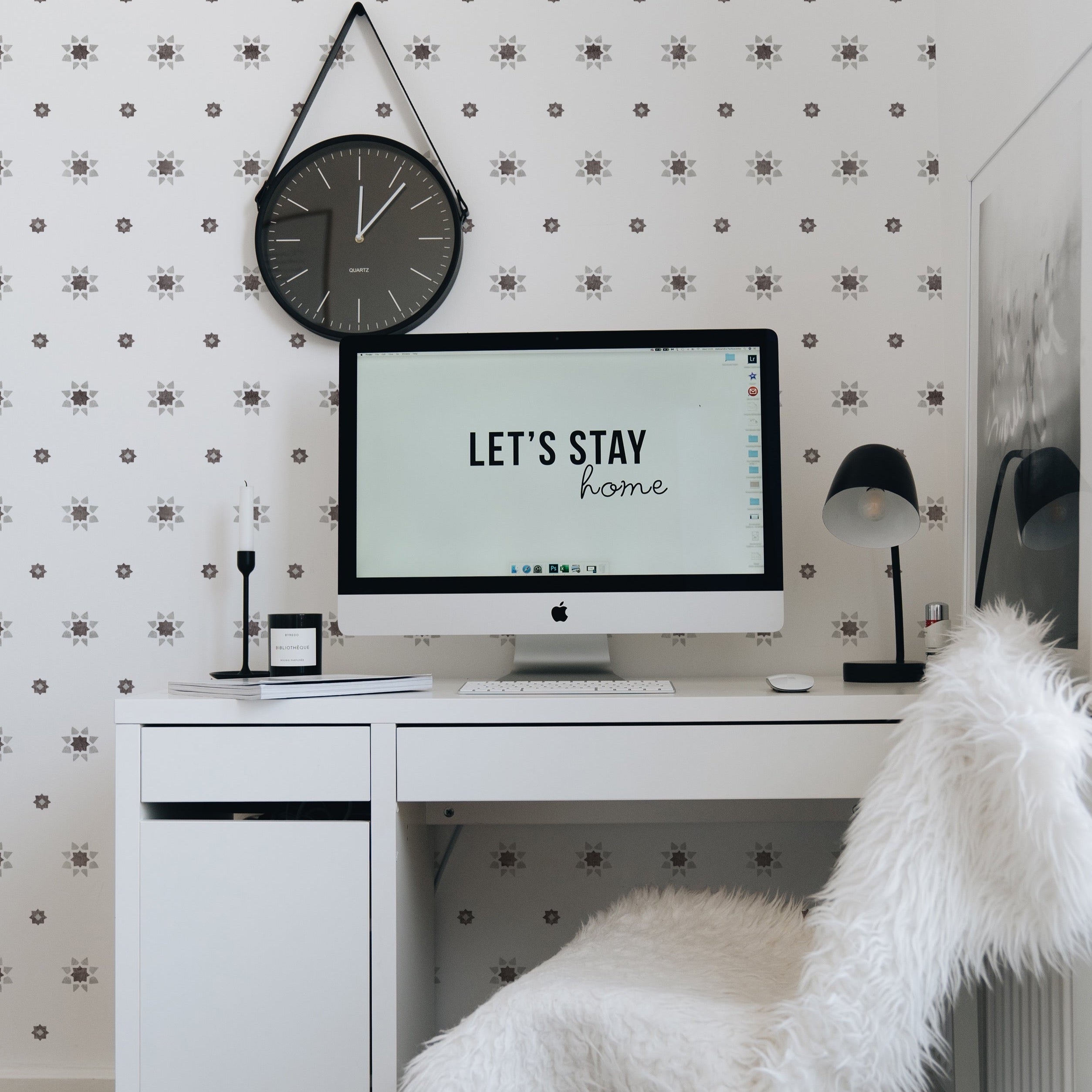 A stylish home office setup with 'Hand Painted Azulejos Wallpaper' featuring a delicate pattern of grey star-shaped designs. The wallpaper adds a subtle yet sophisticated touch to the space, complemented by a modern desk, white fluffy chair, and a wall-mounted clock.