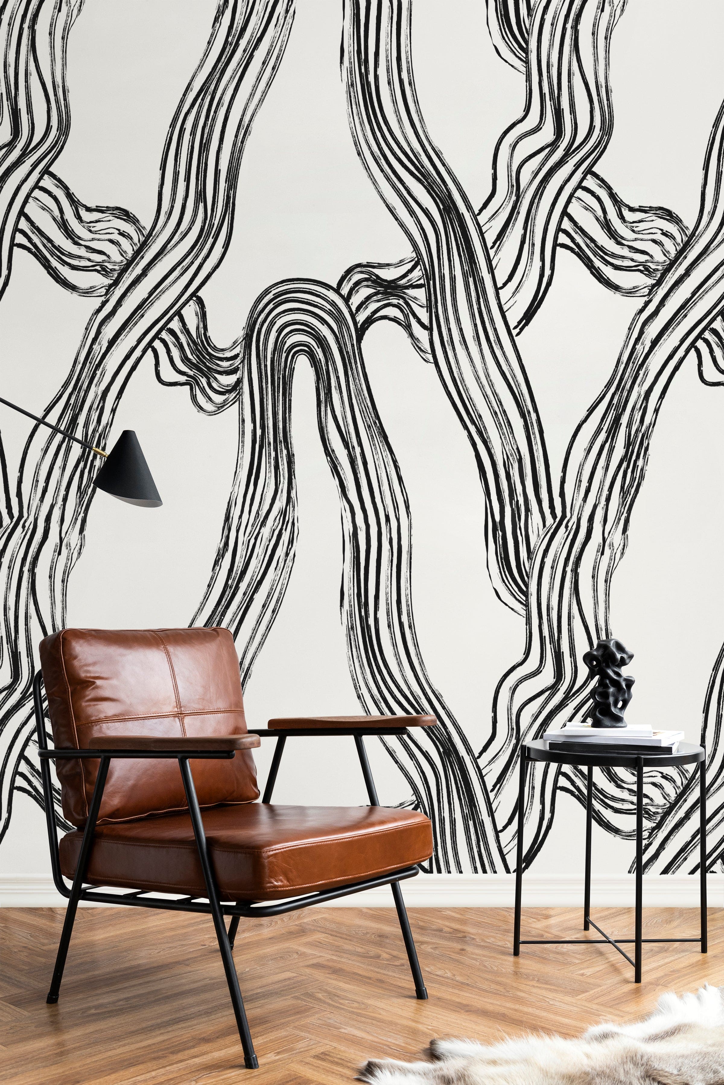Chic interior design with a vintage leather chair against a backdrop of abstract flowing lines wallpaper in black and white. The space is accented by a minimalist side table and a small sculpture, enhancing the artistic flair of the room.