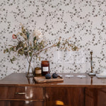  A stylish corner of a home decorated with Charming Floral Wallpaper in Deep Brown. The space features a classic wooden dresser topped with a vase of dried flowers and elegant home accessories, enhancing the wallpaper's vintage floral aesthetics.