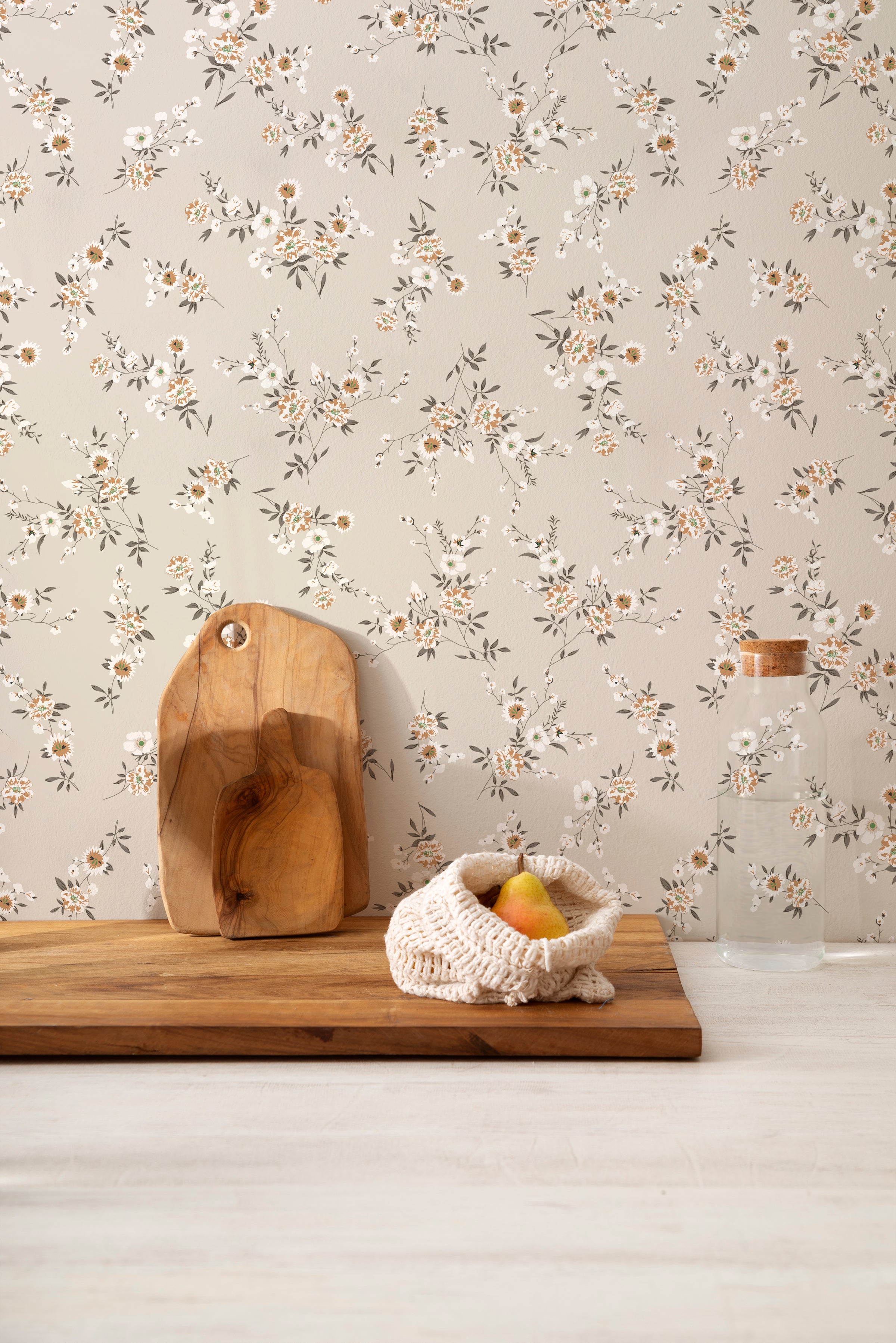 A kitchen countertop against the Classic Floral Wallpaper - Ecru, with a wooden cutting board, glass jar, and a knitted fruit bowl in front, creating a homey and inviting atmosphere.