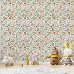 A playful children’s play area with Colourful Spring Bunnies Wallpaper featuring a lively pattern of rabbits, floral motifs, and green foliage. The setting includes soft toys, wooden blocks spelling out the year, and a gray plush rug, creating a whimsical and inviting space for kids