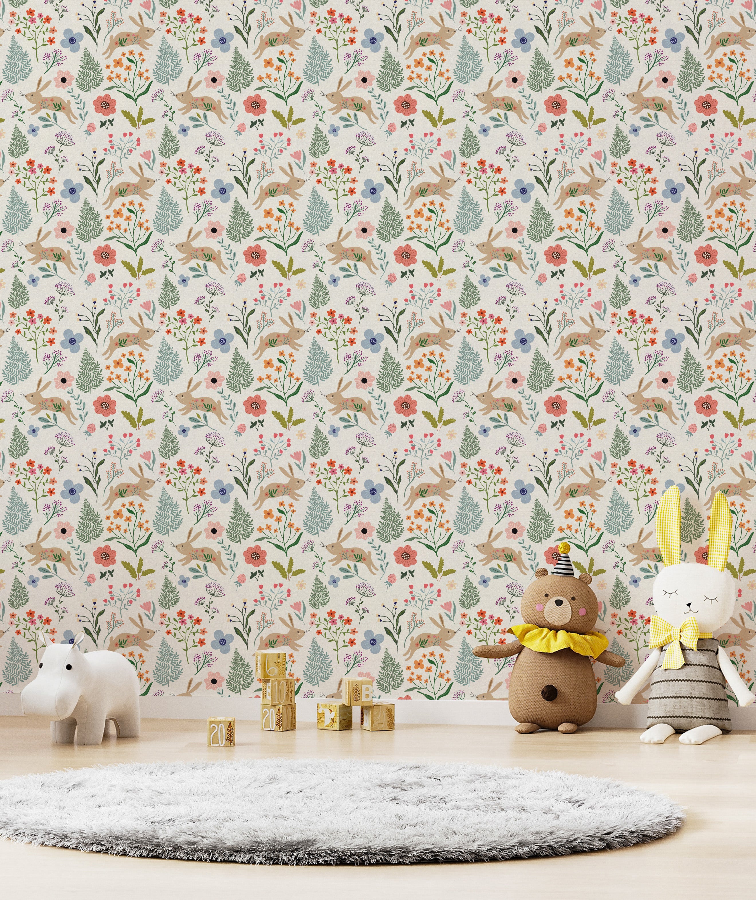 A playful children’s play area with Colourful Spring Bunnies Wallpaper featuring a lively pattern of rabbits, floral motifs, and green foliage. The setting includes soft toys, wooden blocks spelling out the year, and a gray plush rug, creating a whimsical and inviting space for kids