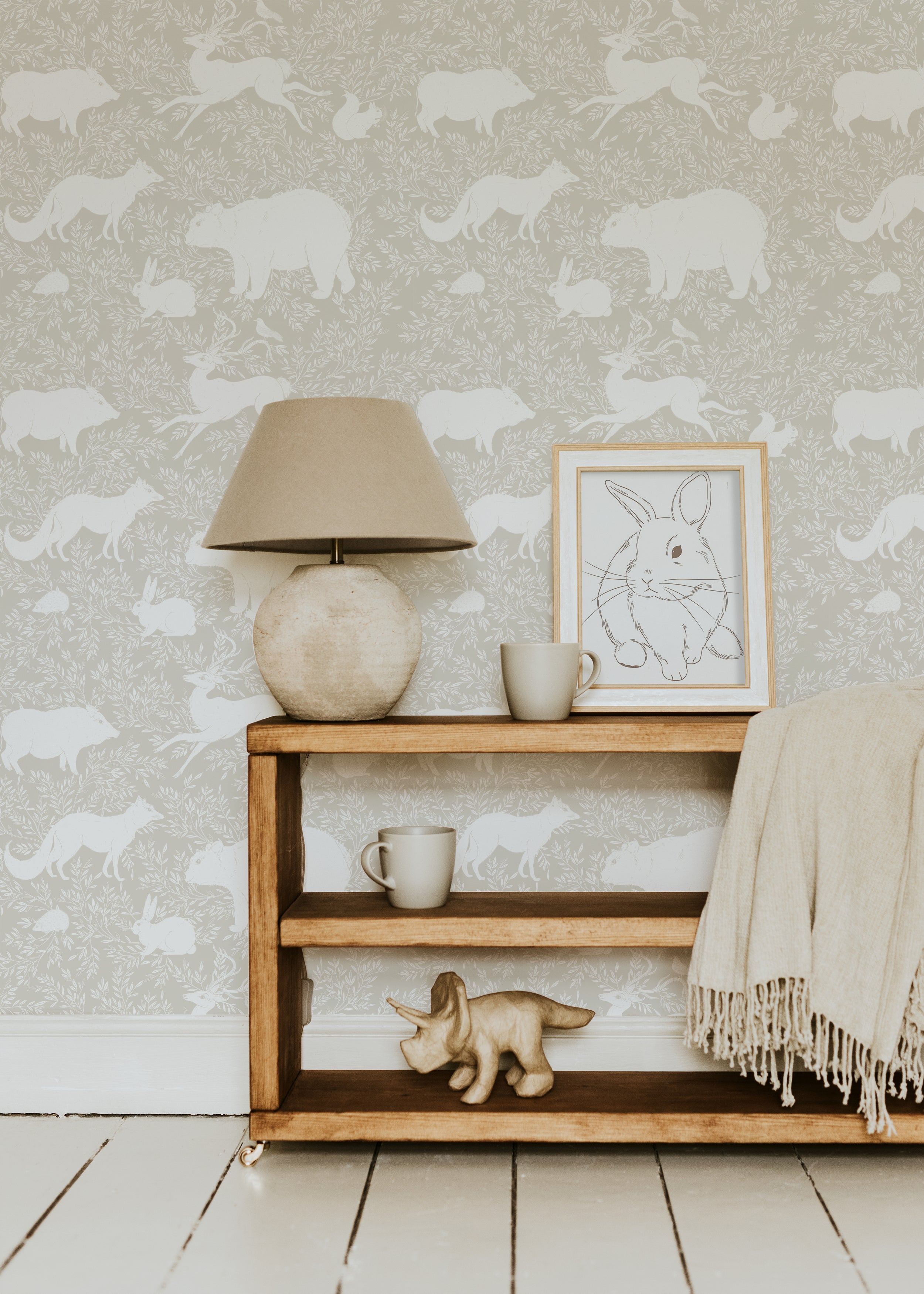 A home office with a light wooden desk and white chair placed against a warm beige wallpaper adorned with white woodland animals including bears, foxes, and rabbits, creating a calming and natural ambiance