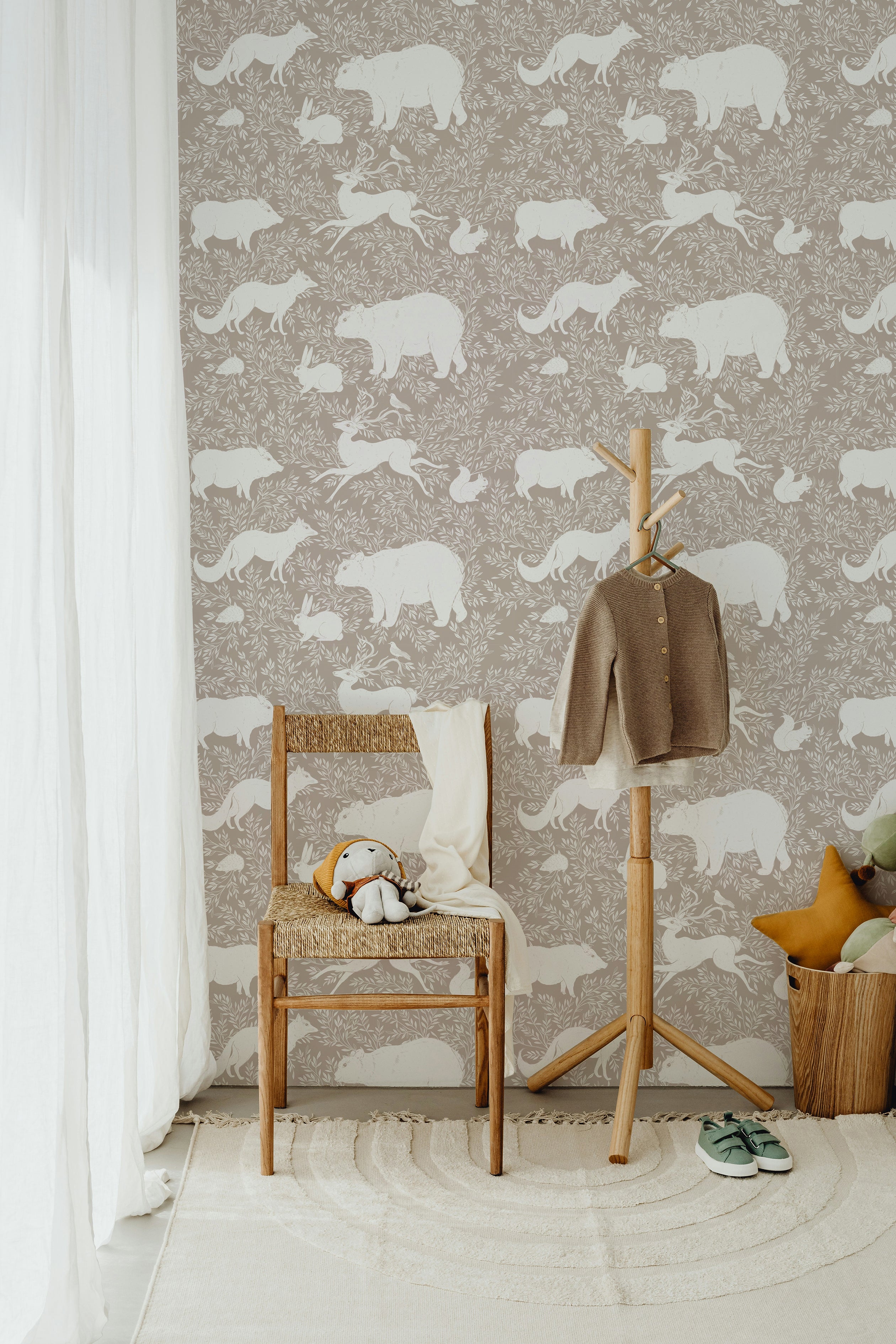 A cozy room with a wooden chair, soft toys, and a hanging coat in front of a beige wallpaper featuring white woodland animals such as bears, foxes, and rabbits, creating a serene and natural atmosphere.