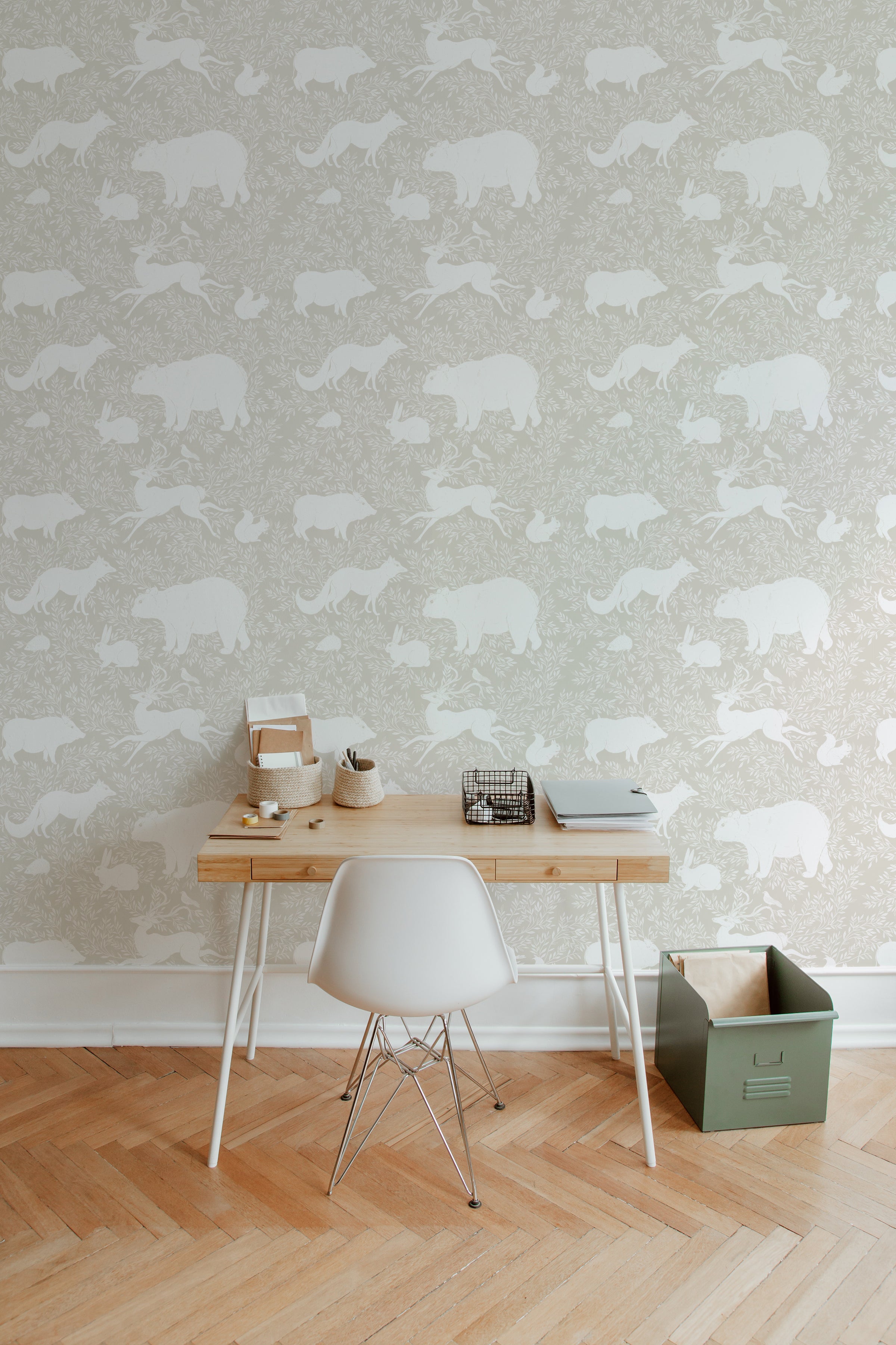 A cozy room with a wooden chair, soft toys, and a hanging coat in front of a warm beige wallpaper featuring white woodland animals such as bears, foxes, and rabbits, evoking a serene and natural atmosphere.