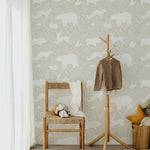 A cozy room with a wooden chair, soft toys, and a hanging coat in front of a warm beige wallpaper featuring white woodland animals such as bears, foxes, and rabbits, evoking a serene and natural atmosphere.