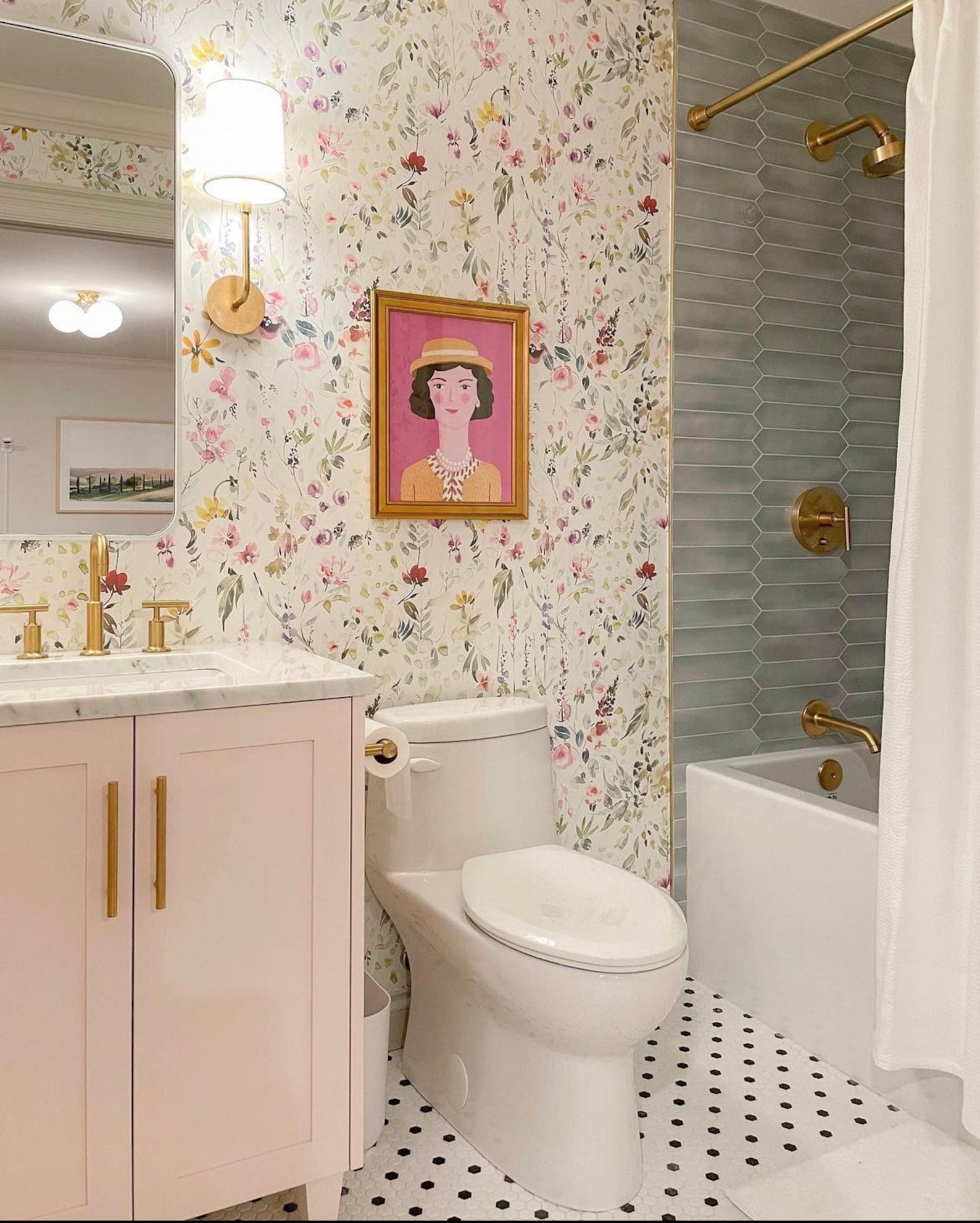 Chic and cozy bathroom interior graced with Hera's Floral Wallpaper, featuring an abundance of watercolor flowers in full bloom against a bright backdrop, paired with pink cabinetry and gold fixtures for a touch of elegance
