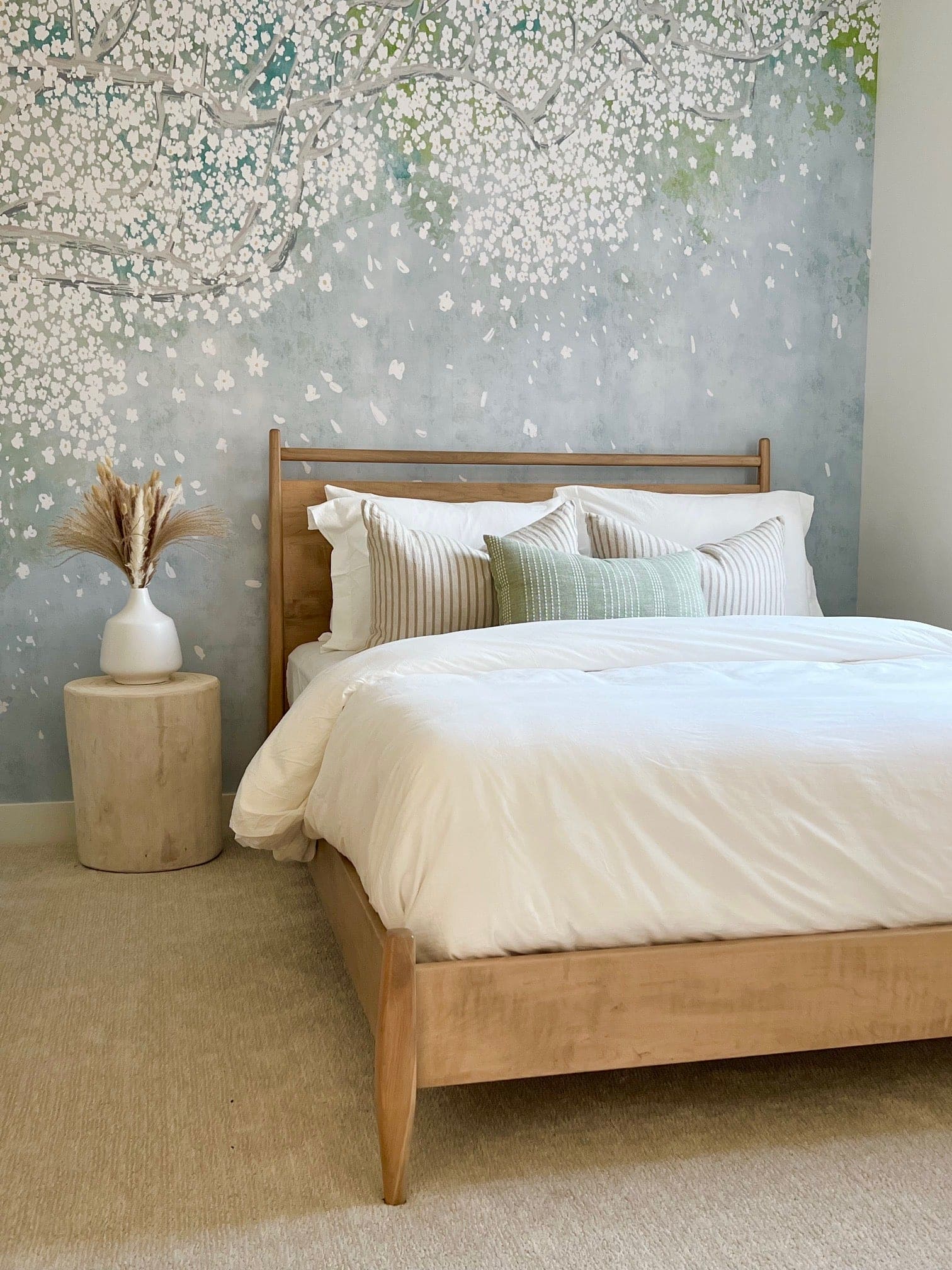 A peaceful bedroom showcasing the cherry blossom mural as a headboard, complemented by soft bedding and neutral decor. The wallpaper's delicate flowers and branches convey a restful ambiance.