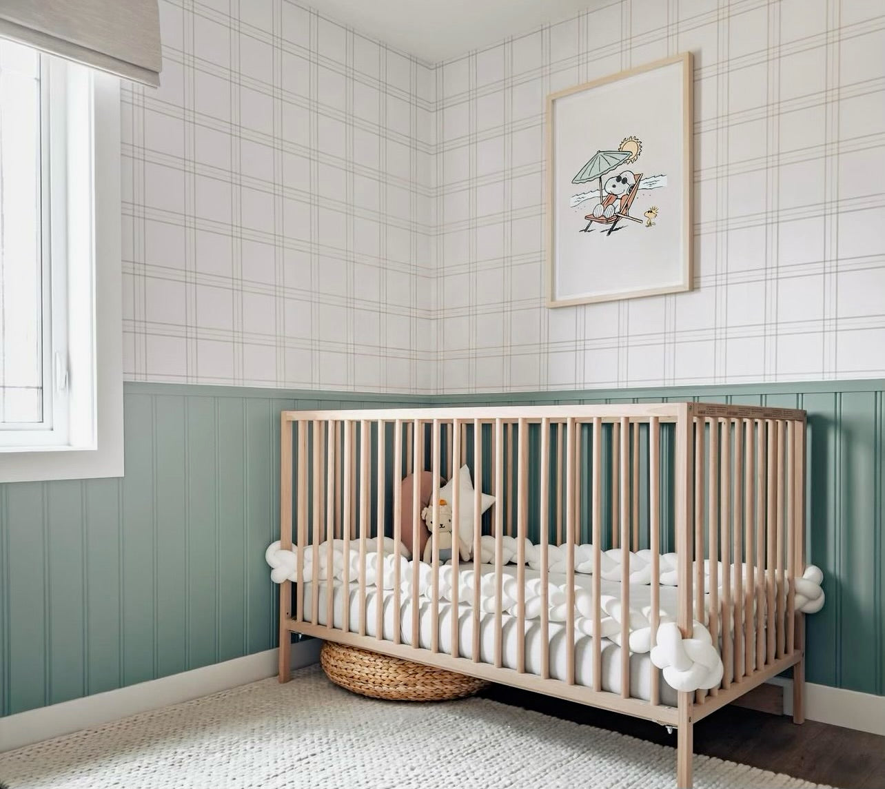 Nursery room featuring Traditional Tartan Plaid Wallpaper with soft gray lines forming a grid pattern, complemented by a lower half wall in green, framing a wooden crib and a playful framed illustration of a bird with an umbrella.