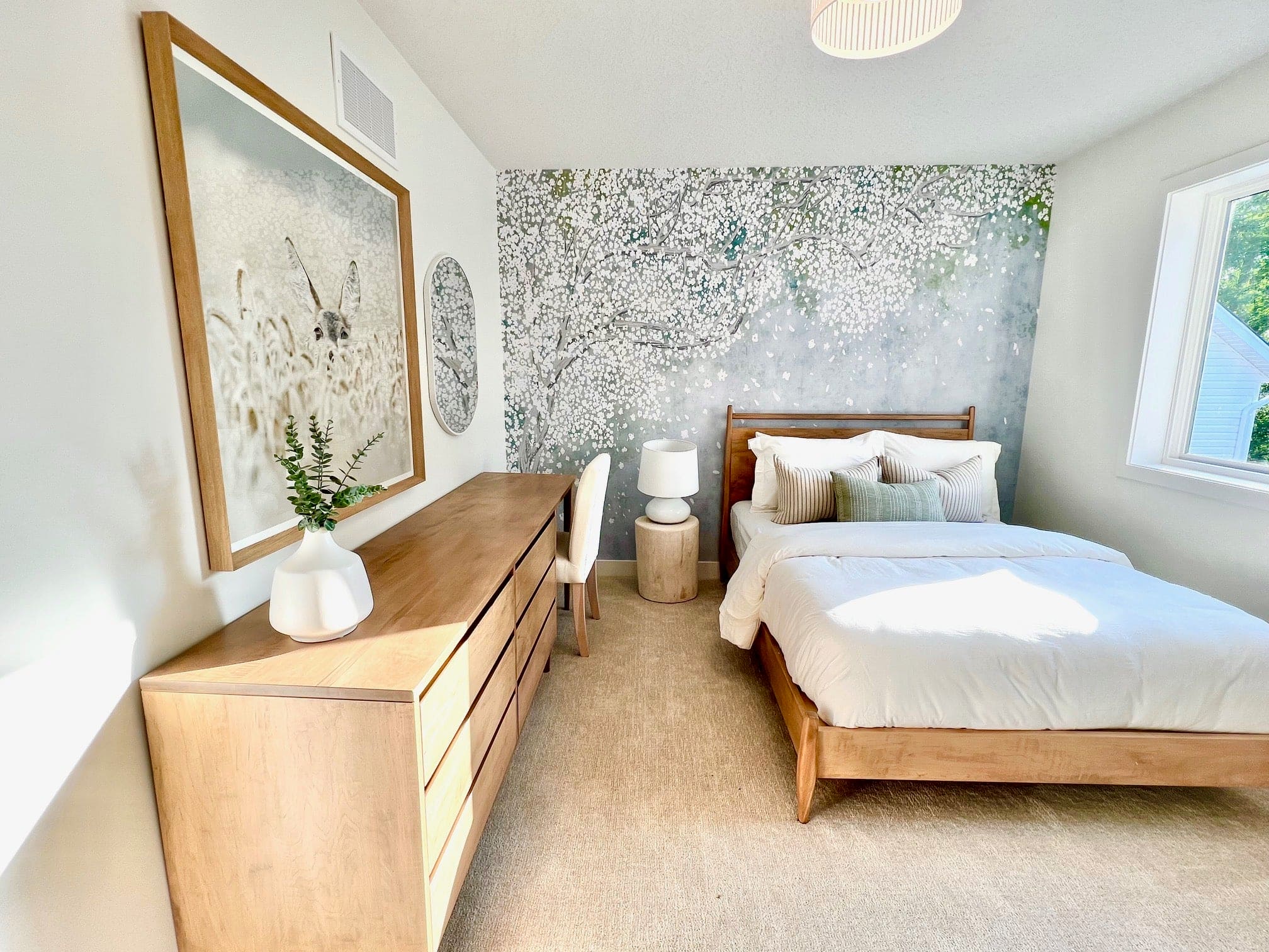 A bright bedroom with a natural wood bed and furniture, accented by the Nursery Mural Wallpaper depicting a lush cherry blossom canopy. The gentle pastel colors of the blooms add a serene and spring-like atmosphere to the room