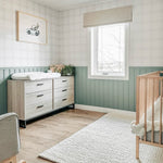 Spacious nursery decorated with Traditional Tartan Plaid Wallpaper, green wainscoting, and wood flooring. The room includes a changing table and artwork of a car, providing a serene yet charming environment for a child.